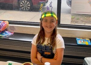 Photo of a child smiling at camera with a robot they built on their head