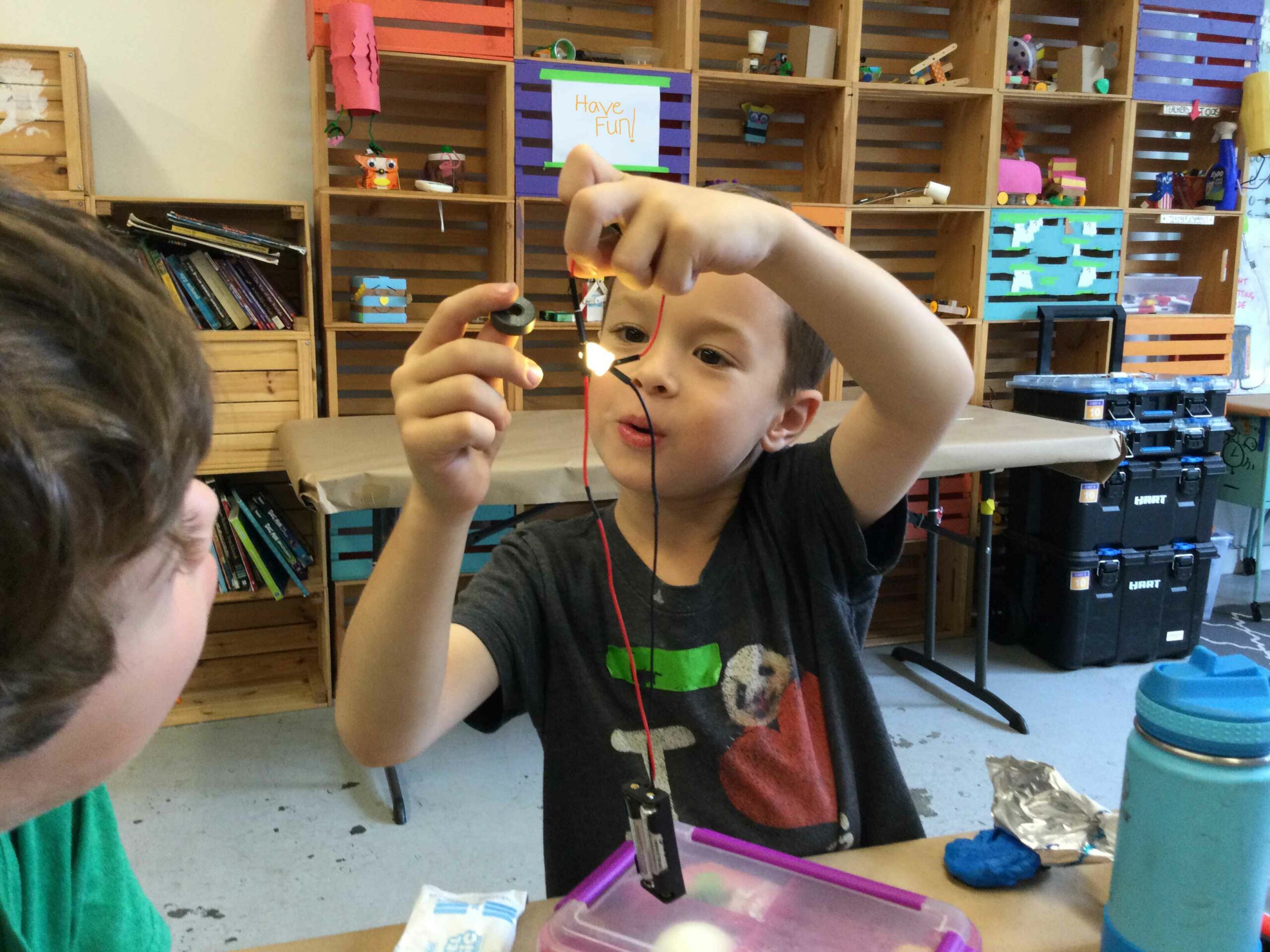 Photo of a child holding up a circuit with a lit LED for another student to see