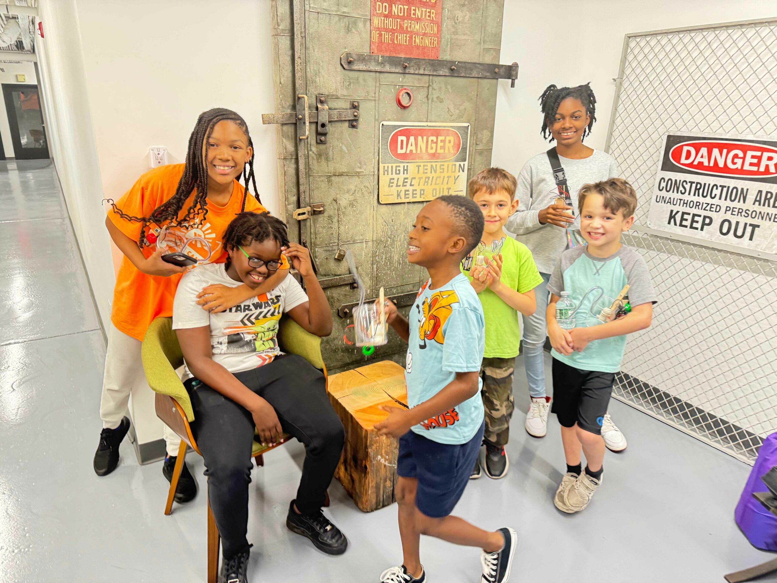 Photo of a group of kids all smiling for camera. They're standing in front of lots of signs that say "Danger"