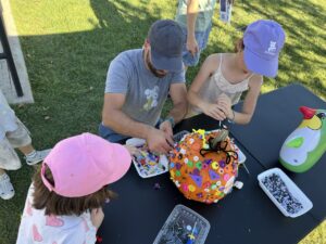 Family decorating a pumpkin with a screwdriver, screws, and colorful decorations at the festival