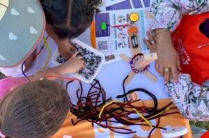 Children creating bracelets with beads and pipe cleaners using the Brace-o-Matic robot, which makes bracelets