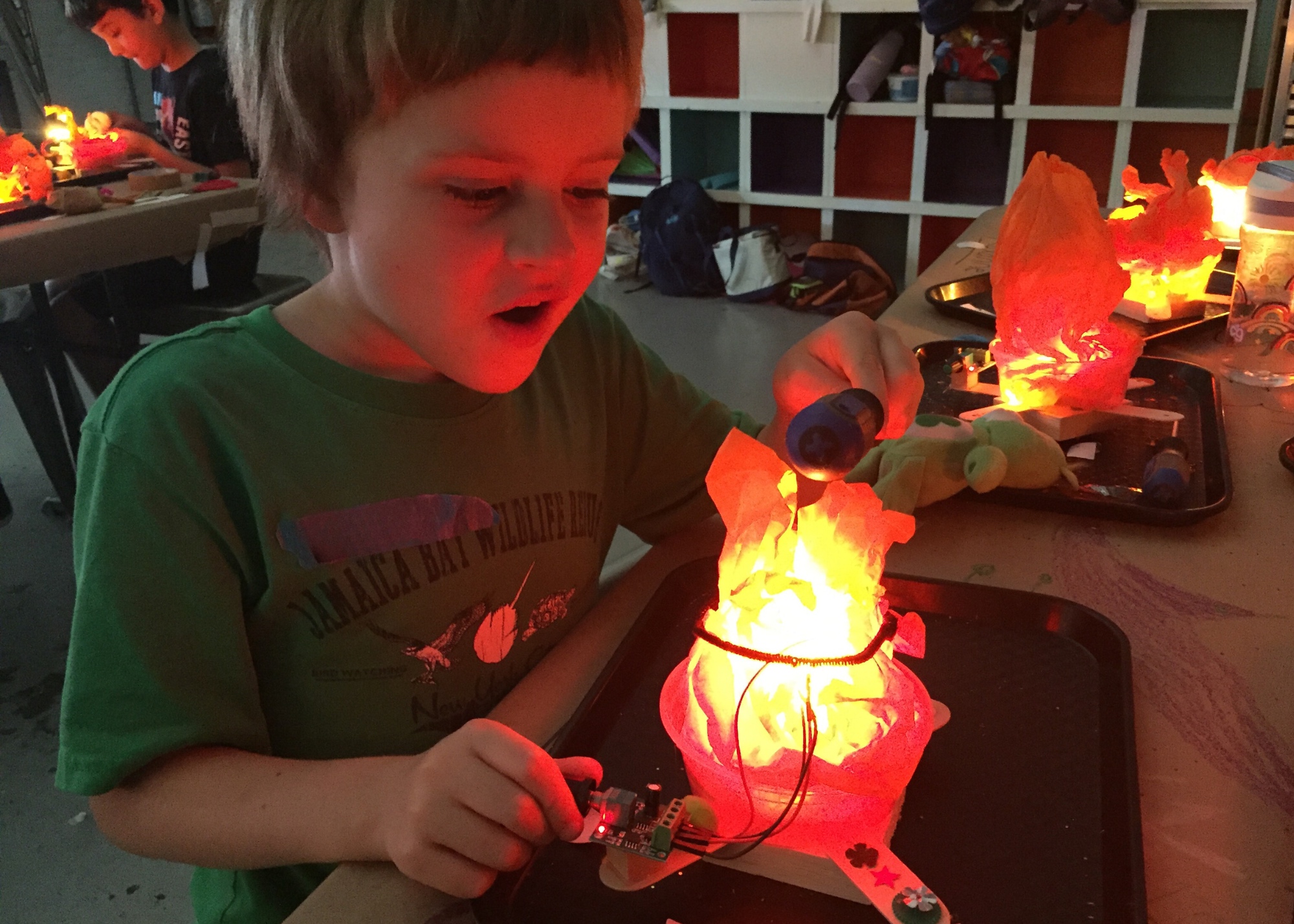 Photo of a student in the dark looking on in amazement at the lit-up fire robot they made