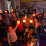 A classroom of kids in the dark, holding up their glowing robots and smiling.