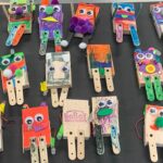 A black table is has approximately 15 kid-made Bitsy Bots lined up on it.