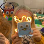 group of children holding up glowing robots they made in front of their faces