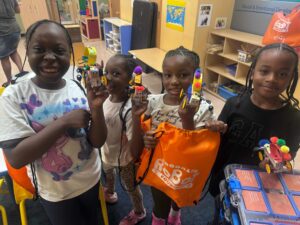 4 children proudly holding up the robots they built and a Brooklyn Robot Foundry bag.